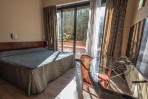 Schlafzimmer mit einem Bett, einem Glastisch und einem Fenster in der Unterkunft Hotel Petra in La Romanina