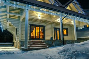 une maison recouverte de lumières de Noël dans la neige dans l'établissement WhiteWood Cottages, à Bukovel