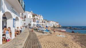 une plage avec des bâtiments blancs et des gens sur le sable dans l'établissement 1Solive - Calella de Palafrugell, à Calella de Palafrugell