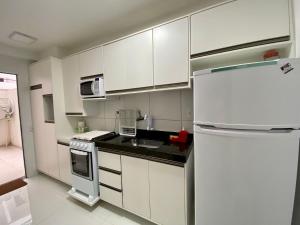 La cuisine est équipée de placards blancs et d'un réfrigérateur blanc. dans l'établissement Jardins de Ilhéus - Apto COMPLETO localização PRIVILEGIADA, à Ilhéus