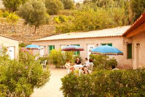 a group of people sitting at a table with umbrellas at Residence San Damiano - Location Appartements, Studios & Chambres in Algajola