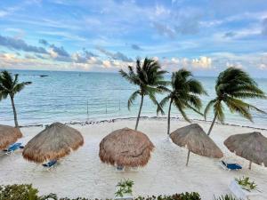 un grupo de sombrillas de paja y palmeras en una playa en All Ritmo by Andiani Travel en Cancún