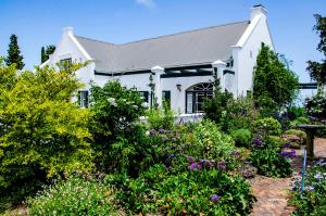 a white house with a garden of flowers at Greenhill Farm Manor House Plettenberg Bay - Private House Sleeps 8 in Plettenberg Bay
