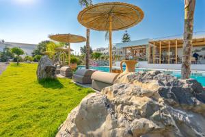 a resort with a pool and an umbrella and some rocks at Kouros Home & Suites in Faliraki