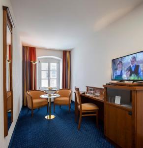 um quarto de hotel com uma mesa e cadeiras e uma televisão em Altstadthotel der Patrizier em Regensburg