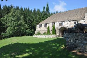 an old stone building with a green field and trees at Domaine du Lac Ferrand in Saint-Cirgues-en-Montagne