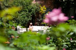 a woman sitting on a couch in a garden at Dar Rhizlane, Palais Table d'hôtes & SPA in Marrakech