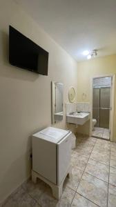 baño con lavabo y TV en la pared en Pousada Vale do Ouro Verde, en Serra Negra