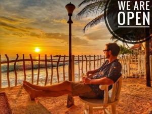 un hombre sentado en una silla en la playa viendo la puesta de sol en Hikka Sandy Pearl Beach Resort, en Hikkaduwa