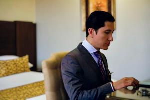Um jovem de fato e gravata a olhar para o relógio. em Hotel Patrimonio em Cuenca