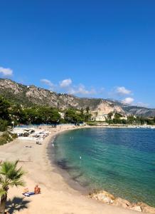 a beach with people laying on the sand and the water at Les Jasmins in Beaulieu-sur-Mer