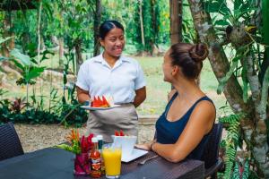 Una donna che tiene un piatto di cibo accanto a una donna seduta a un tavolo di Bocawina Rainforest Resort a Hopkins