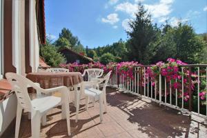 eine Terrasse mit weißen Stühlen, einem Tisch und rosa Blumen in der Unterkunft Willa Pałacyk in Świeradów-Zdrój