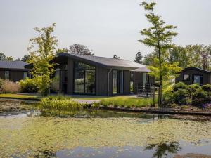 a house with a pond in front of it at Beautiful chalet with a bath, in a holiday park in the Brabant Kempen in Veldhoven