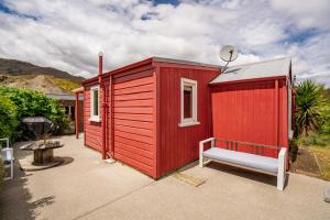 a red tiny house with a bench in a yard at Cromwell Cutie - Cromwell Holiday Home in Cromwell