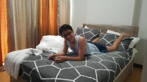 Uma mulher deitada numa cama a olhar para o telemóvel. em Room in Studio - Mesaverte Residences Afs Suites em Cagayan de Oro