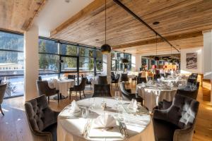 restauracja z białymi stołami i krzesłami oraz dużymi oknami w obiekcie Croce Bianca Leisure & Spa Hotel w mieście Canazei