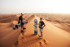 Due uomini sono nel deserto con gli skateboard di Chegaga Nomad Camp a El Gouera