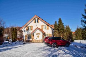 a red car parked in front of a house in the snow at Konie2 Pokoje Gościnne in Wetlina