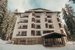 a large white building in the snow with trees at Max Holiday Apartment in Pamporovo