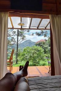 a person laying on a bed in front of a window at Cabana Arbosana in São Bento do Sapucaí
