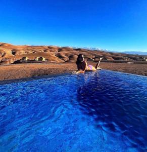 a woman sitting in a pool of blue water at Agafay Luxury camp in Marrakech