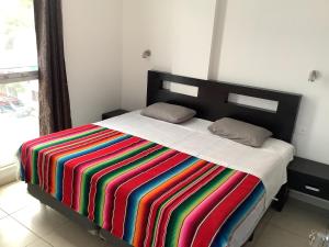 Una cama con una manta de rayas de colores. en Condo Kiaraluna en Playa del Carmen