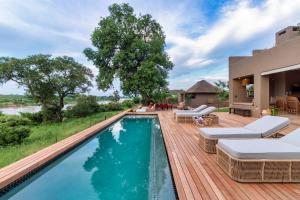 a swimming pool on a deck with chairs and a house at Ukuthula House in Hectorspruit