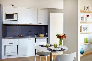 a kitchen with white cabinets and a white table and chairs at Citadines Presqu'île Lyon in Lyon