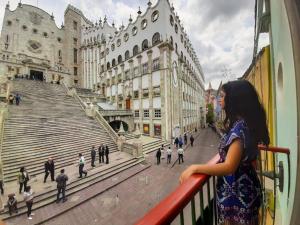 a woman standing on a balcony looking out at a city at Hotel de la Paz in Guanajuato