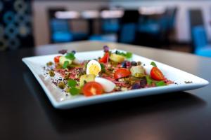 a white plate with a salad on a table at The Grand Winnipeg Airport Hotel by Lakeview in Winnipeg +19 photos
