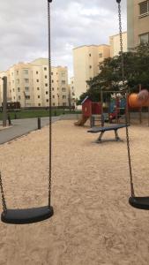 um parque infantil com dois baloiços e um escorrega em شقة في مدينة الملك عبدالله الاقتصادية حي الشروق em King Abdullah Economic City