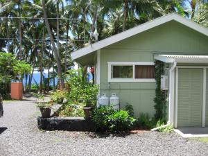 a green house with a garage and palm trees at Whale House at Kehena Beach in Pahoa