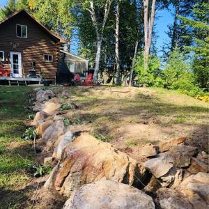 a yard with rocks in front of a log cabin at Le chalet au souvenir in Bouchette