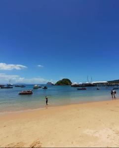 two people standing on a beach with boats in the water at Apart Coração de Búzios in Búzios