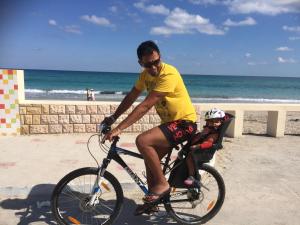 a man riding a bike on the beach with a child at Mahdia - Baghdadi - Laourient Apartments, restaurant, café in Mahdia