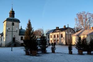 un bâtiment avec une tour d'horloge et des arbres dans une cour dans l'établissement Vadstena innerstad, à Vadstena