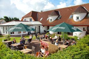 Un groupe de personnes assises à des tables sous des parasols verts dans l'établissement Ferienhotel Bernstein, à Trassenheide