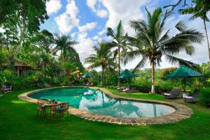 - une piscine avec une table, des chaises et des palmiers dans l'établissement Alam Sari Hotel Keliki, à Ubud