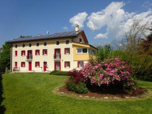 a large white house with red shutters and a bush with pink flowers at Casa Novecento "Rooms & apartments" in Feltre