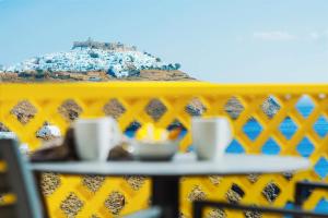 une table avec des tasses sur une clôture jaune avec une montagne dans l'établissement Aelia Apartments & Suites, à Livadi Astypalaias