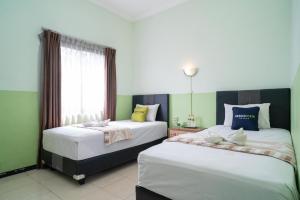 2 camas en una habitación con verde y blanco en Urbanview Hotel de Kopen Malang by RedDoorz, en Malang