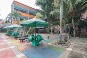 eine Terrasse mit grünen Stühlen und Sonnenschirmen sowie einem Spielplatz in der Unterkunft Urbanview Hotel Sagara Bogor in Bogor