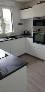 a kitchen with white cabinets and a black counter top at Maison moderne plein coeur de Ouistreham in Ouistreham