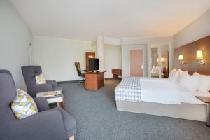 a hotel room with a large bed and chairs at Holiday Inn München Süd, an IHG Hotel in Munich