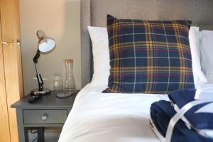 a bed with a plaid pillow and a lamp on a table at Canal view 2 bed picturesque cottage with log fire in Blisworth