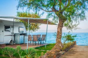 a caravan with a table and chairs under a canopy next to the water at Armenistis Camping & Bungalows in Sarti