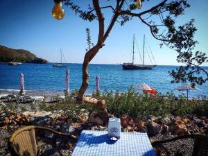 a table and chairs on a beach with a boat in the water at Datca Masal Gibi Plaj&Restaurant in Datca