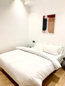 a white bed with white sheets and a painting on the wall at Luxe Parisien - Petit Varenne in Paris