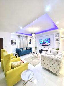 a living room with yellow and white furniture and a tv at Morak Homes - Luxury 4 bed home with PS5, 24hrs electricity, Super fast Wifi, Snooker, Games room - in a secured estate in Abuja